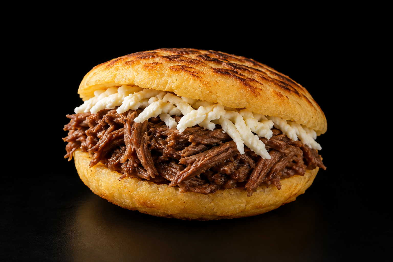 Referencia visual de una arepa venezolana con carne y queso sobre fondo negro